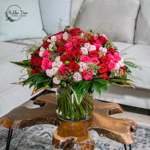 Luxurious dome of red and blush roses with fern on a live edge table by a luxury florist Cary